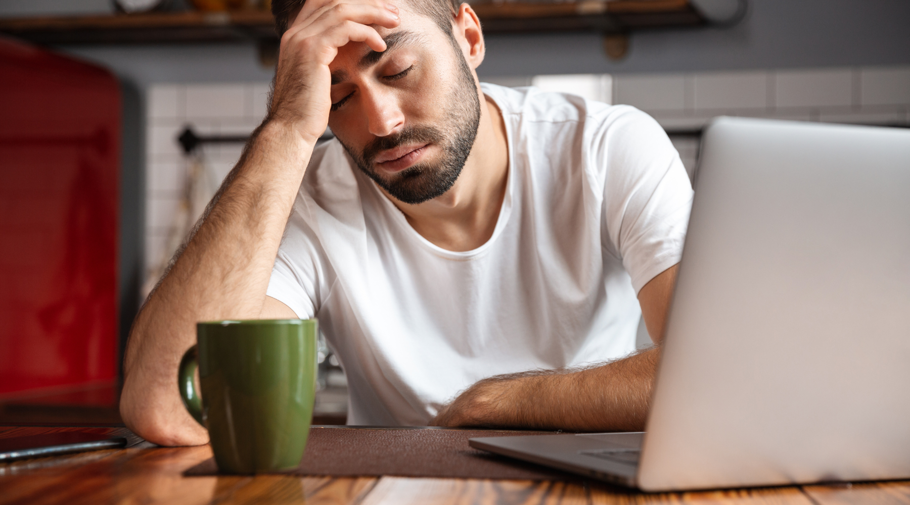 Young white male looking tired at his desk with a cup of coffee