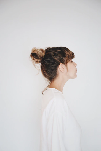 Profile of a woman with hair in a bun, wearing a white shirt, looking thoughtful against a plain background.