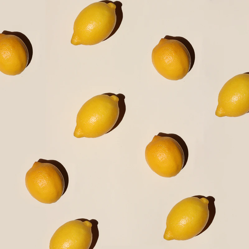 Several whole yellow lemons casting shadows on a light beige surface.