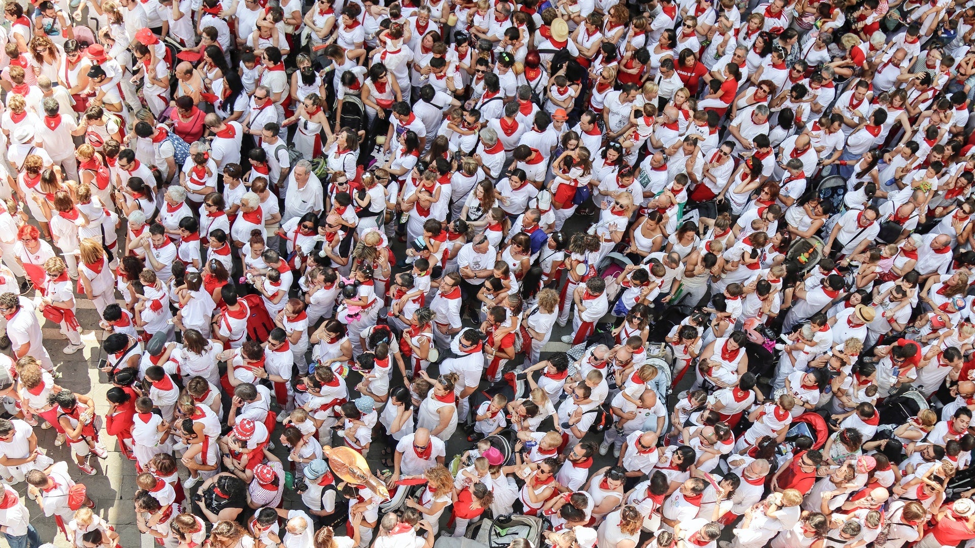 A large crowd of people wearing mostly white clothes with red scarves, viewed from above.