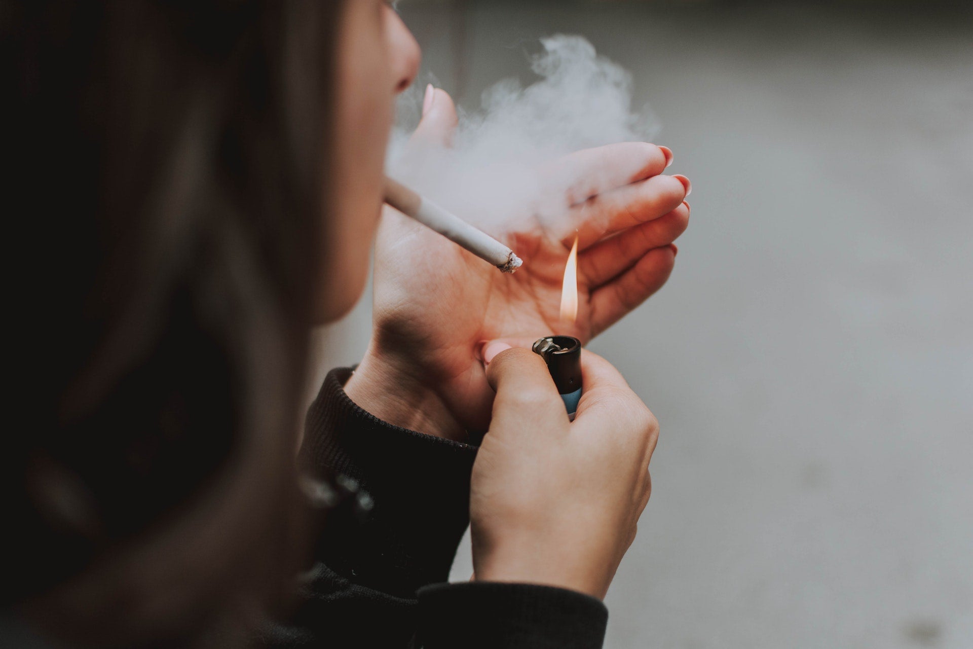 Person lighting a cigarette with a lighter, smoke visible near the cigarette tip, illustrating smoking as a bad habit to break.