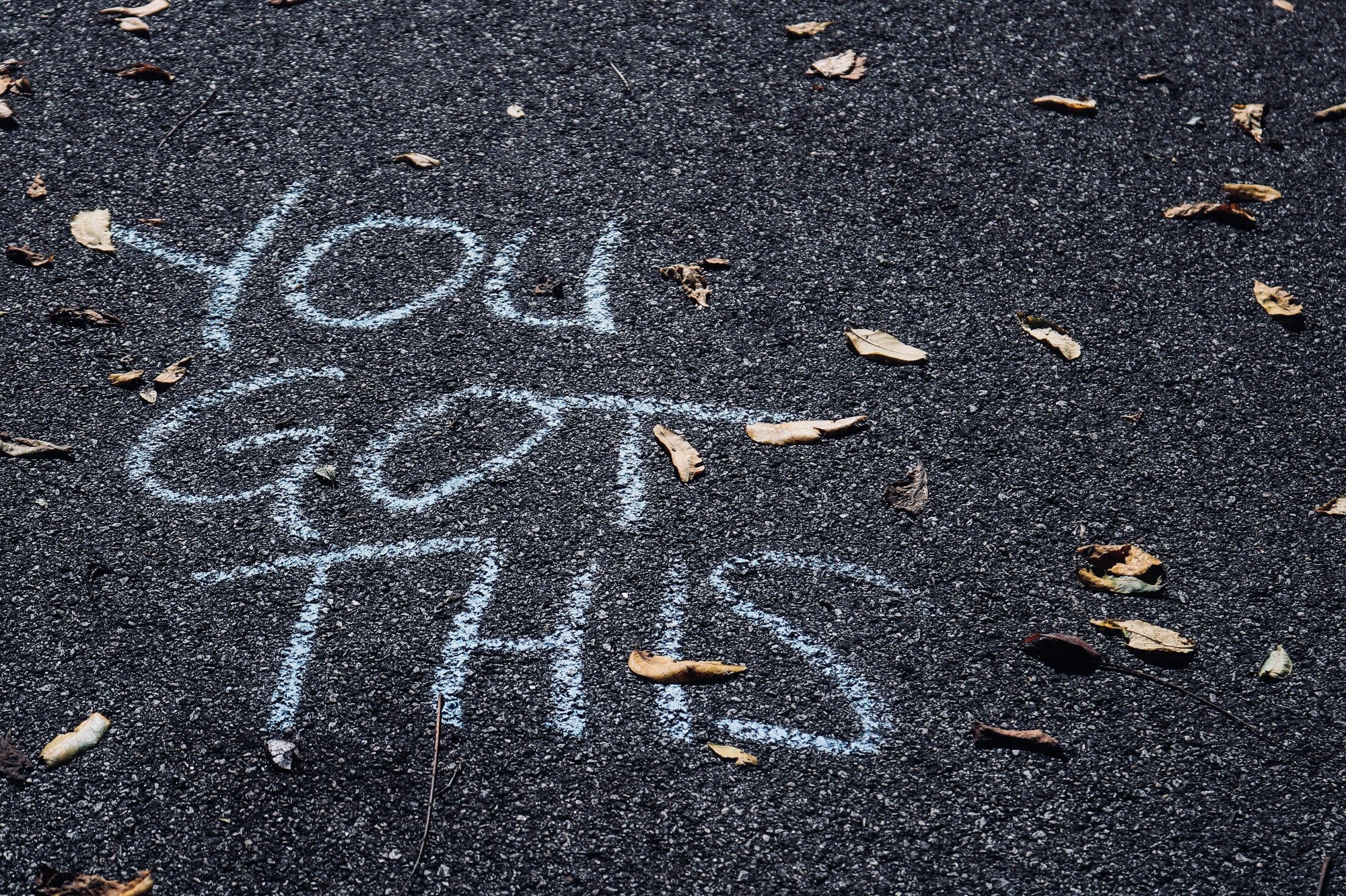 Chalk message on asphalt reads: "You GOT THIS" with scattered dry leaves around.