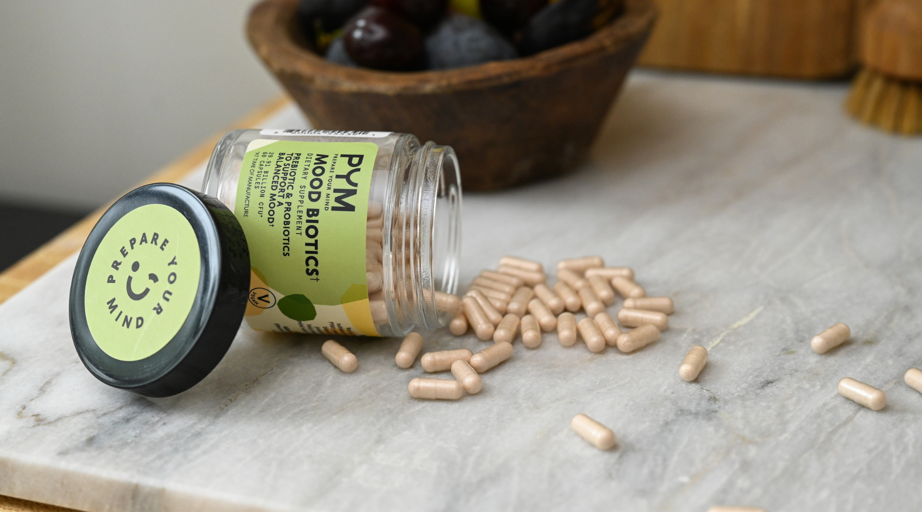 PYM Prepare Your Mind Mood Biotics dietary supplement bottle lying on its side with capsules spilled on a marble surface.