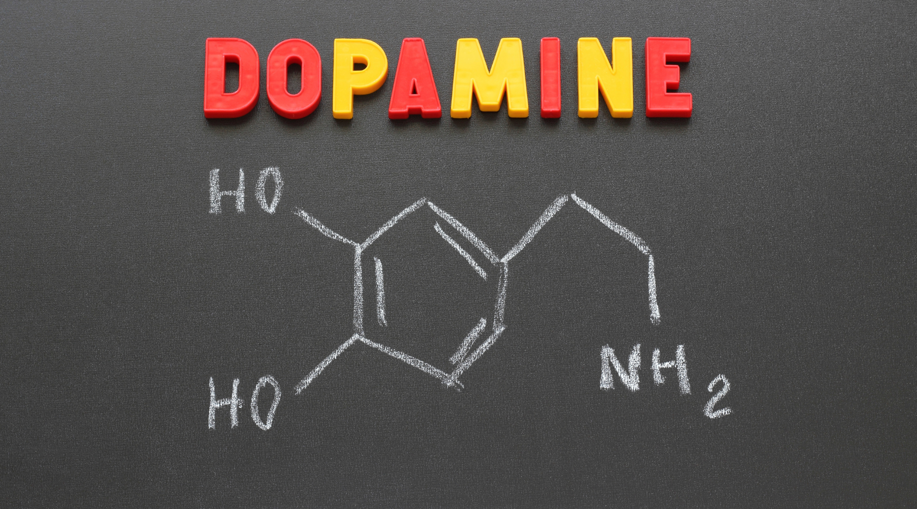 DOPAMINE spelled in red and yellow letters above a chalk drawing of dopamine's chemical structure with labels HO, HO, and NH2 on a blackboard