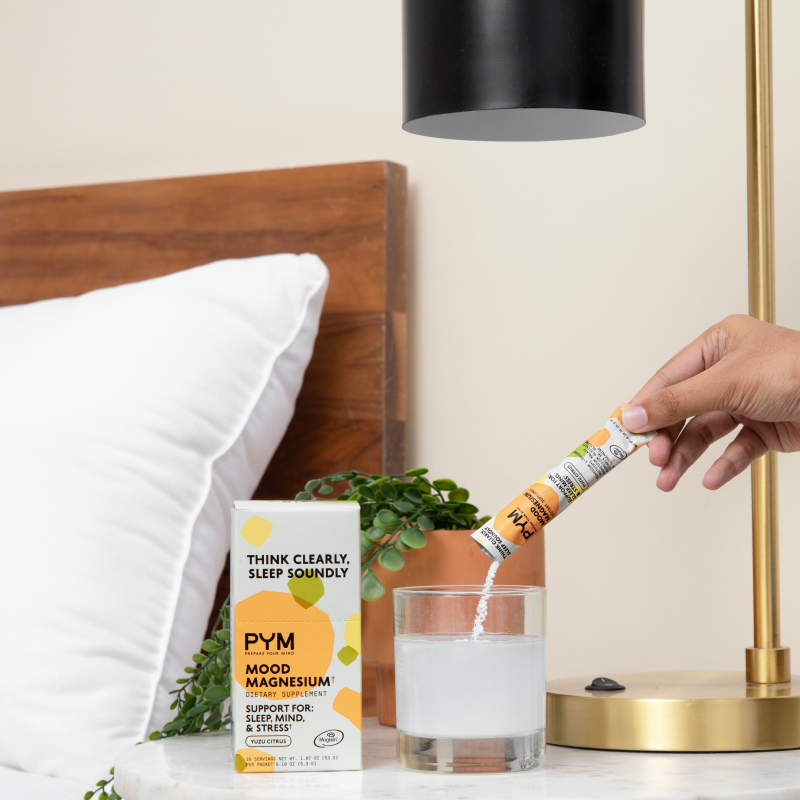 Hand pouring PYM Mood Magnesium dietary supplement powder into a glass of water next to the product box with text: THINK CLEARLY, SLEEP SOUNDLY, PYM MOOD MAGNESIUM, DIETARY SUPPLEMENT, SUPPORT FOR: SLEEP, MIND, & STRESS, YUZU CITRUS.