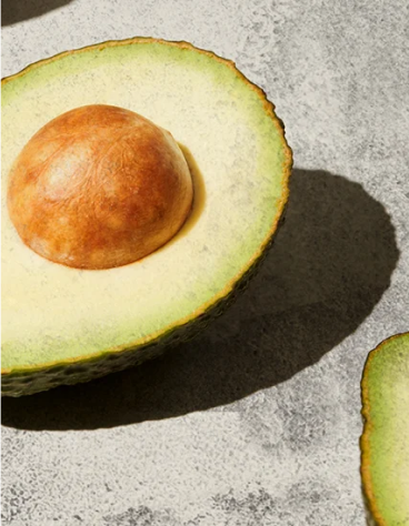 Halved avocado with seed on a textured gray surface, showing the green flesh and brown seed.