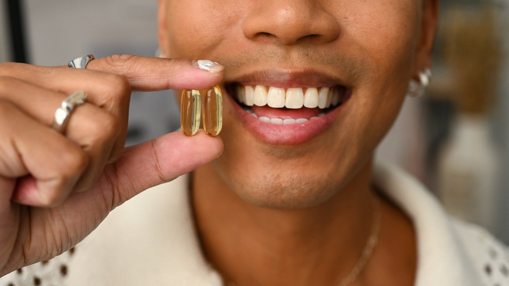 A man smiles and holds up two omega-3 supplements