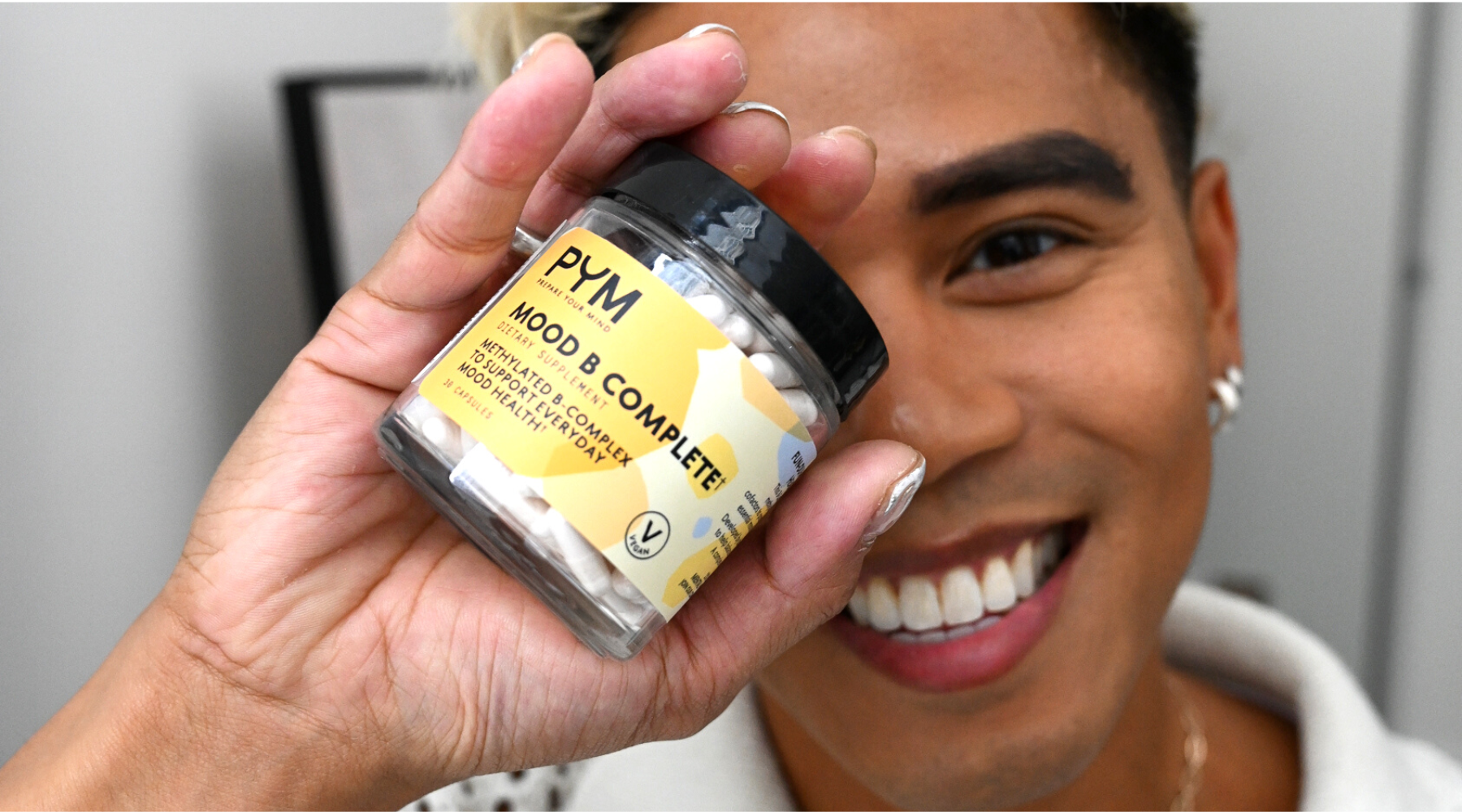 An asian man smiling and holding a jar of mood B complete vitamins
