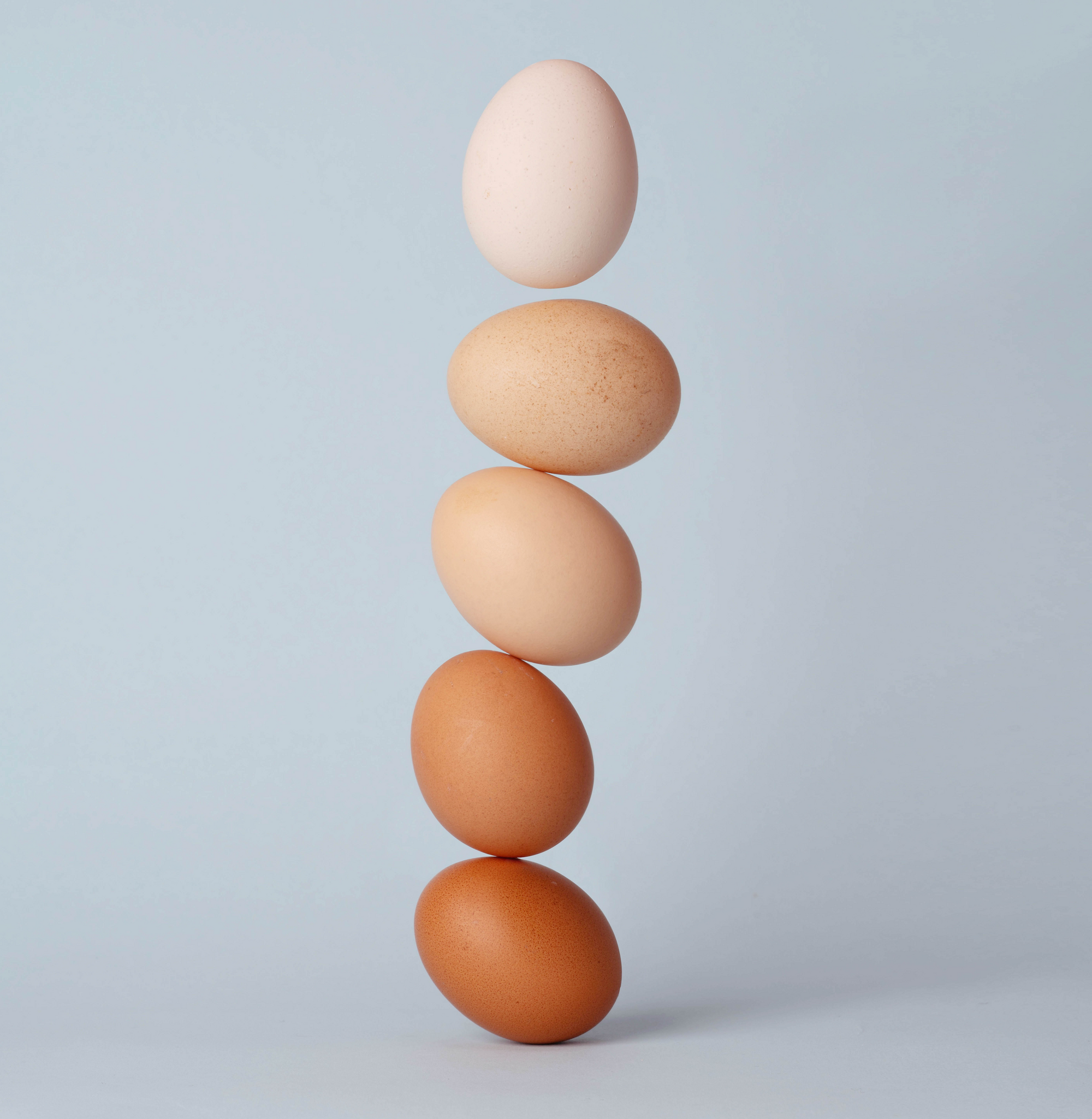 Five eggs stacked vertically in varying shades from light to dark against a pale blue background.