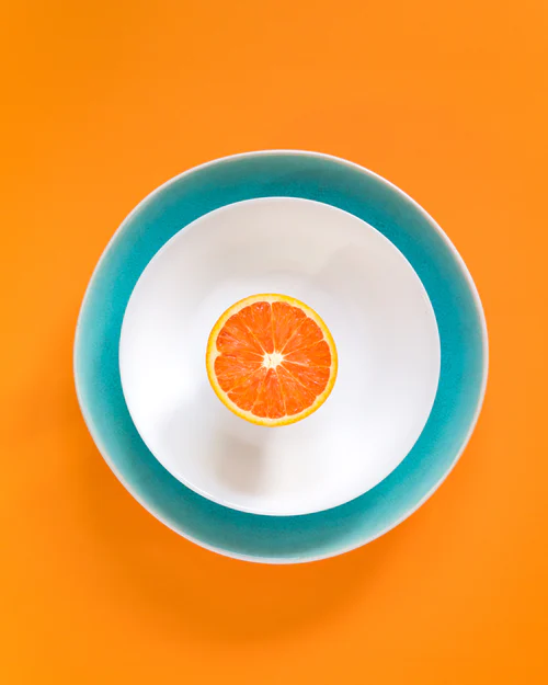 Top view of a sliced orange half on a white plate with a teal rim against an orange background.