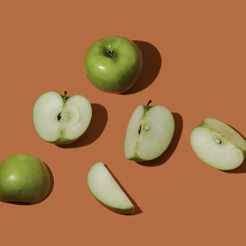 Whole and sliced green apples arranged on a brown surface.