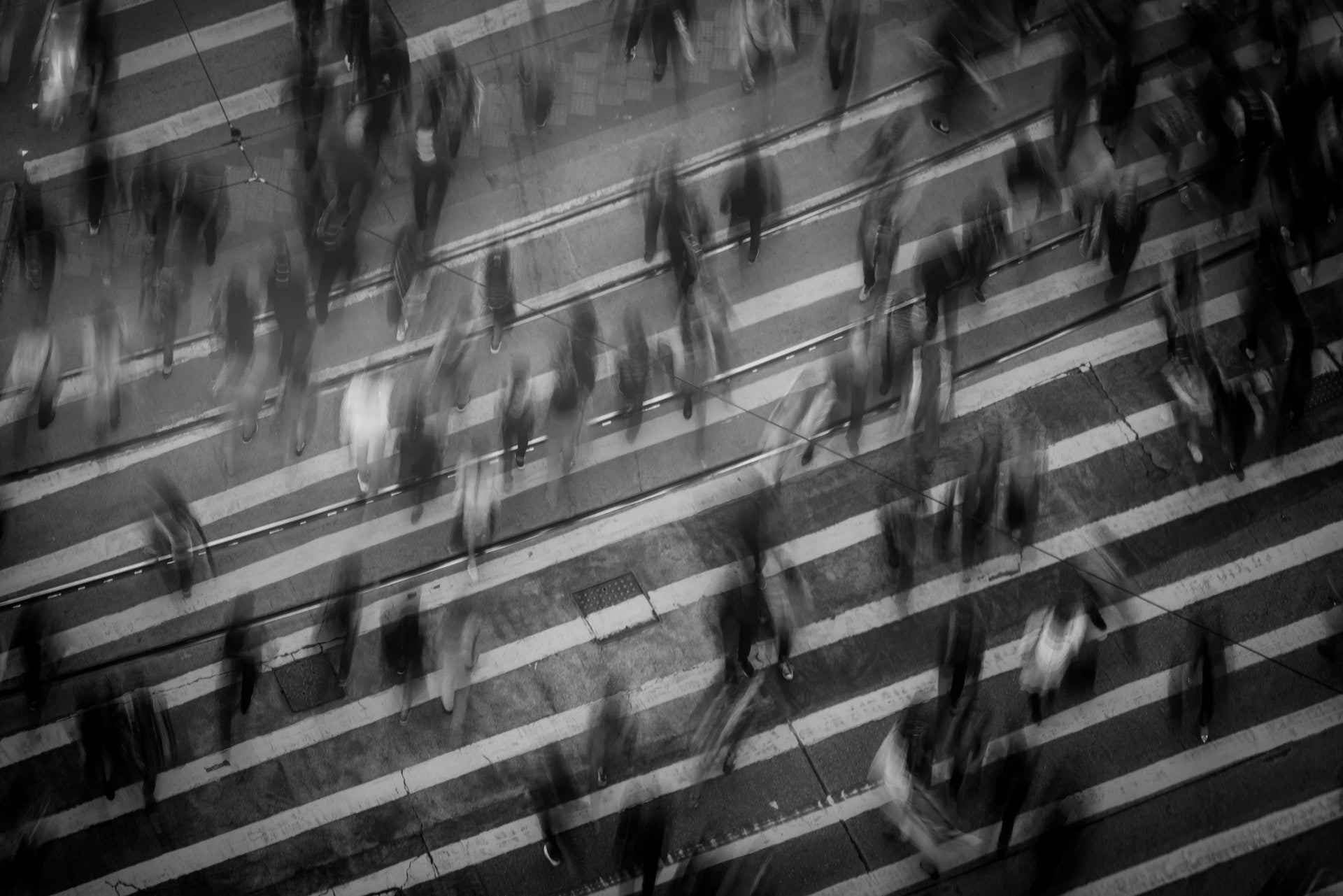 Blurred black-and-white photo of people crossing a street with white pedestrian lines, conveying a sense of social anxiety and crowd overwhelm.