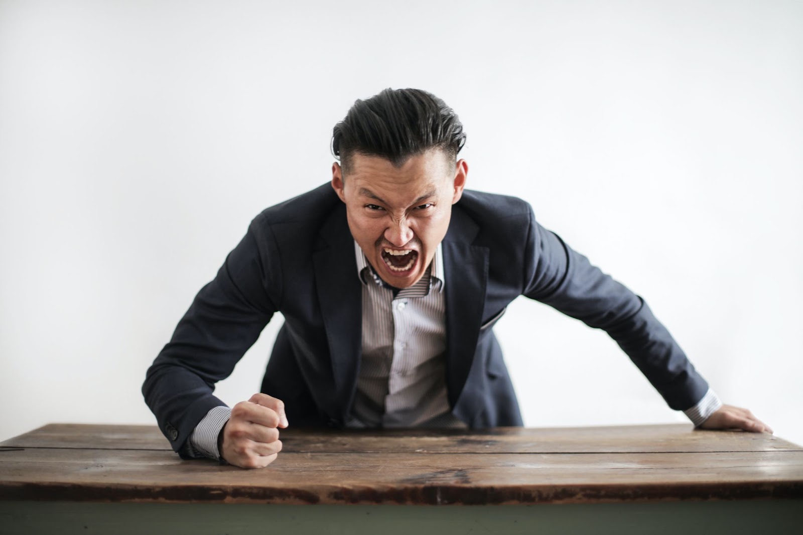 Angry man in a suit pounding a wooden table with a fist, expressing frustration or bad mood