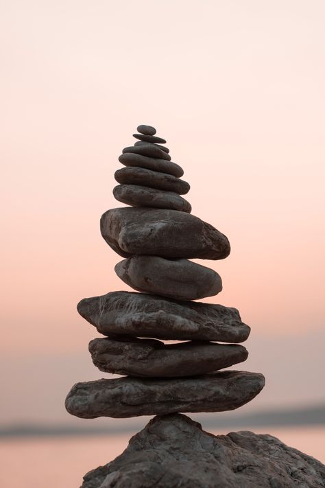 Stack of smooth stones balanced vertically against a soft pink sunset sky over water.
