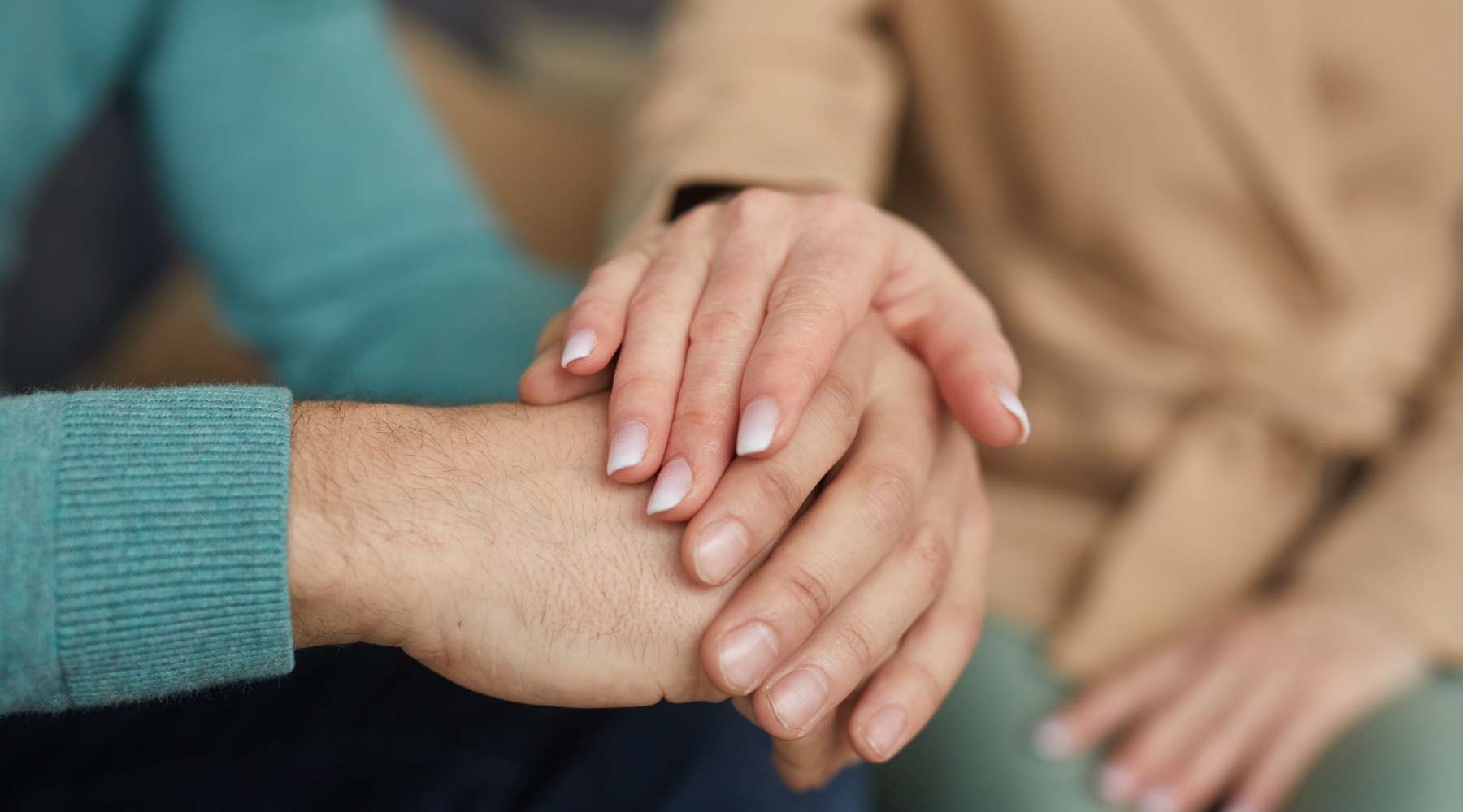 A woman's hand on top of a man's hand showing empathy and support