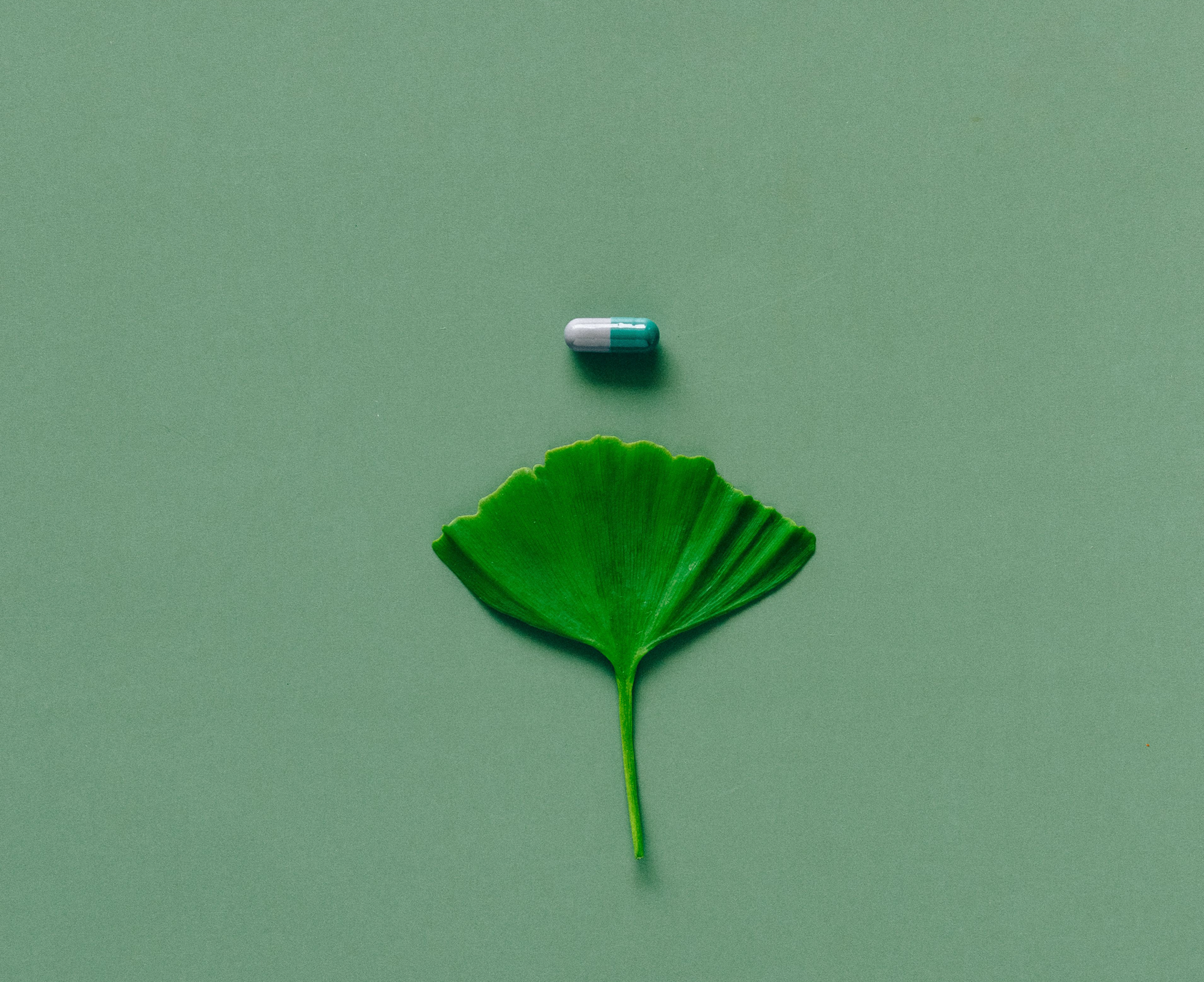 a natural leaf below a pill on an all green background