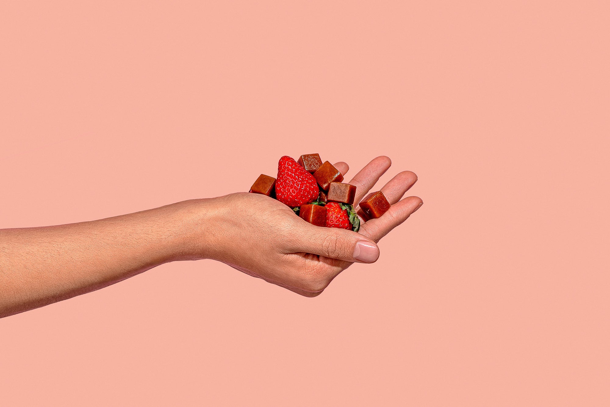 Hand holding PYM Mood Chews and Strawberries on pink background showcasing micronutrients for brain health.