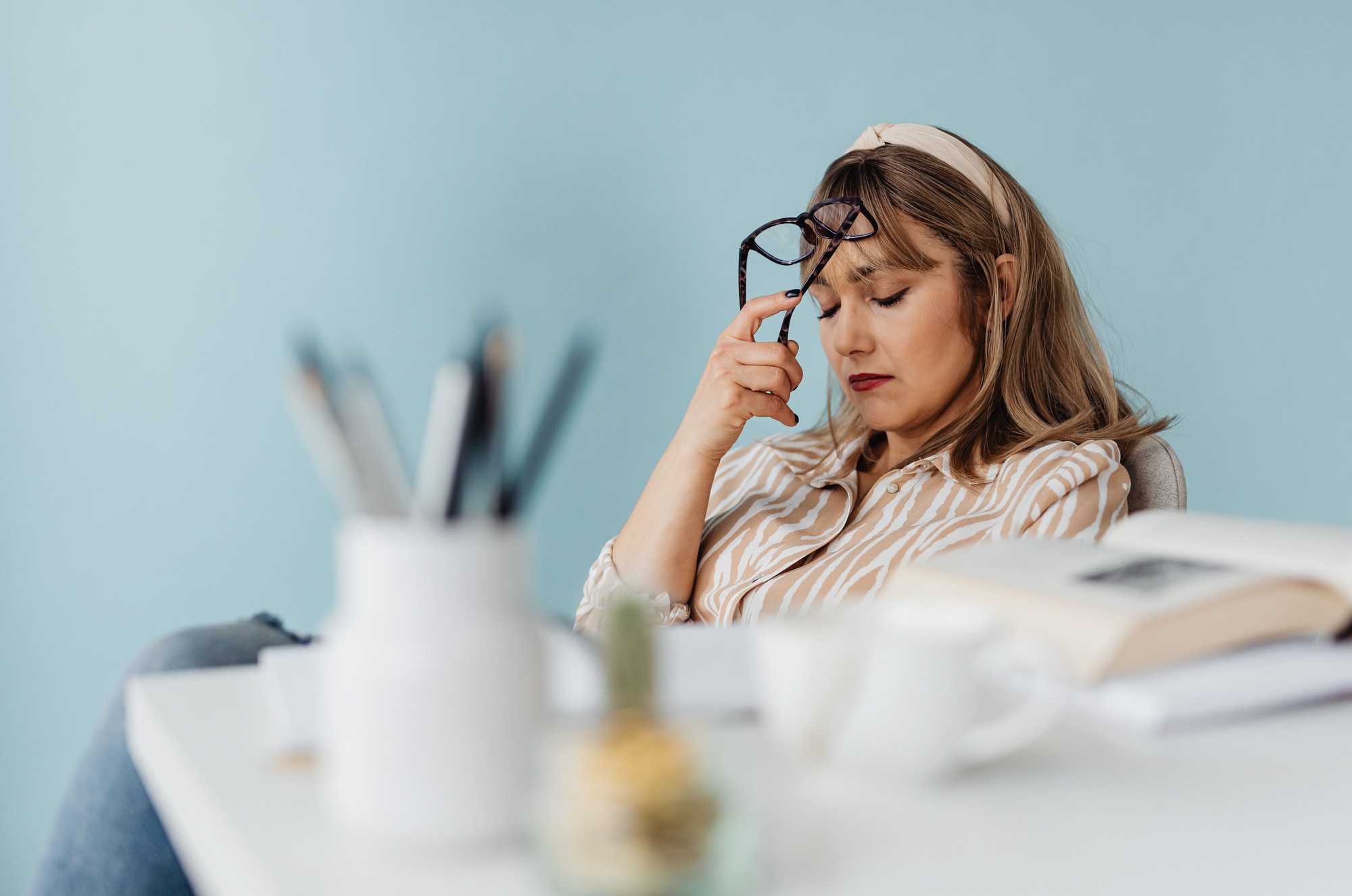 Women with glass pressed to head in front of messy desk