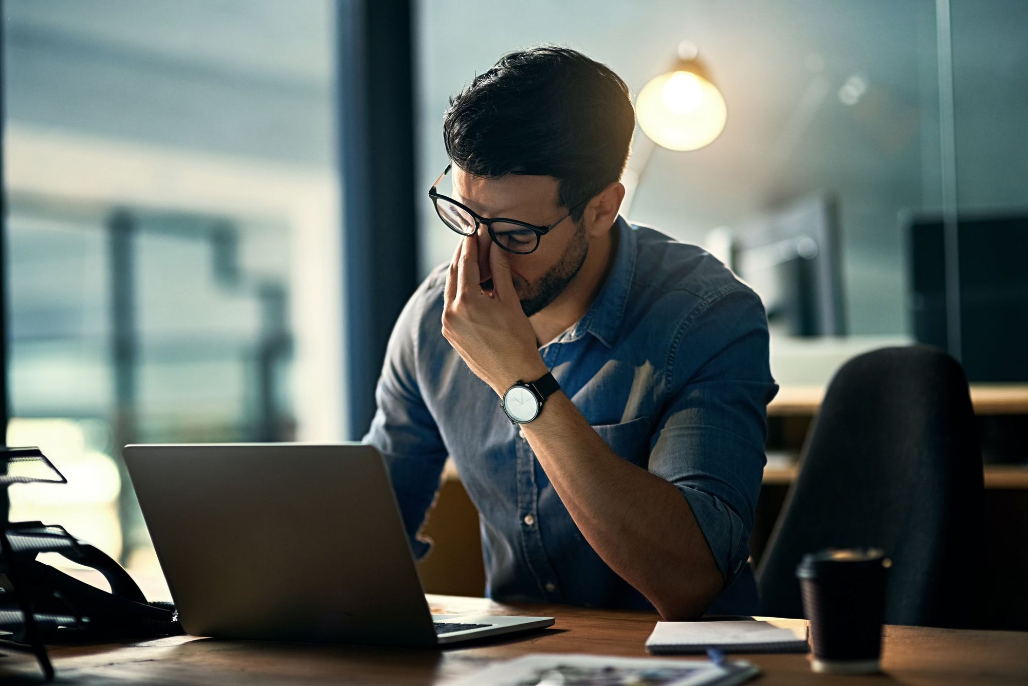 A man looks stressed as he rubs his eyes and looks at his laptop.
