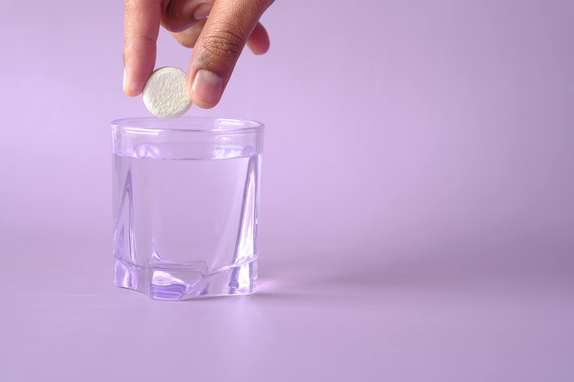 Hand dropping magnesium supplement into a glass of water on a purple background
